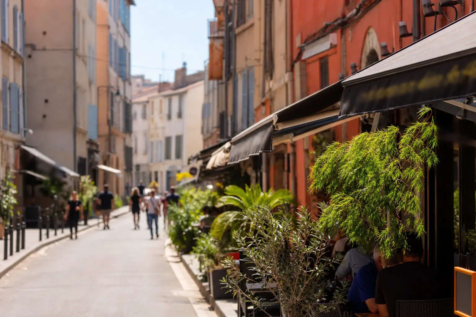 Rue commerçante animée d’un quartier marseillais, façades colorées, terrasses ombragées